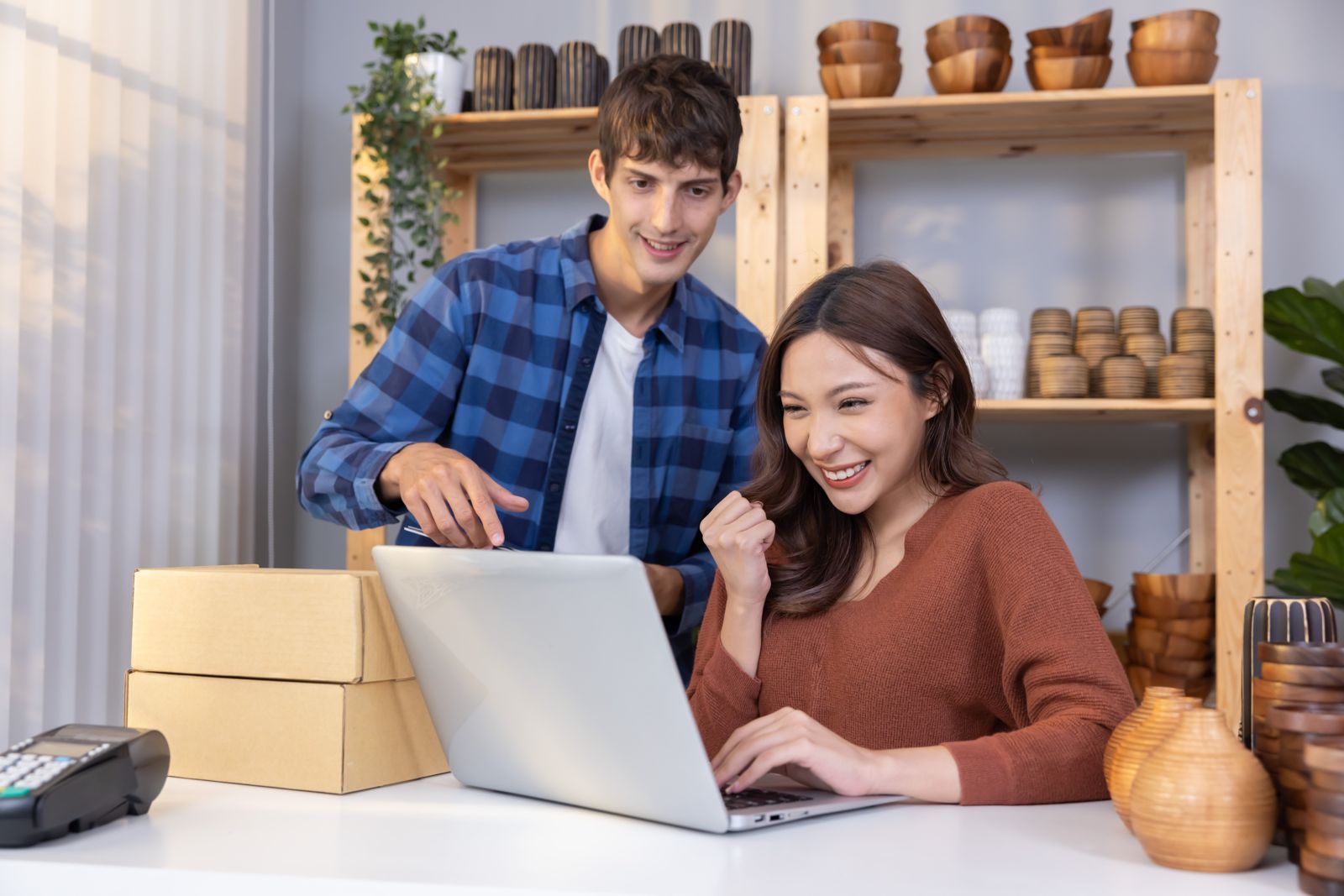 Two online shop owners celebrating a new sale at their laptop beside packed orders